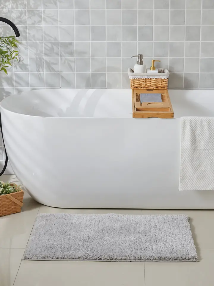 Grey plush bath mat beside a freestanding tub