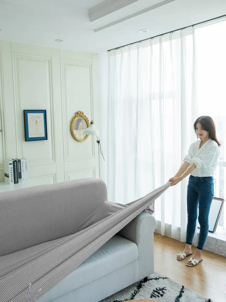 Grey stretch slipcover being fitted over a sofa